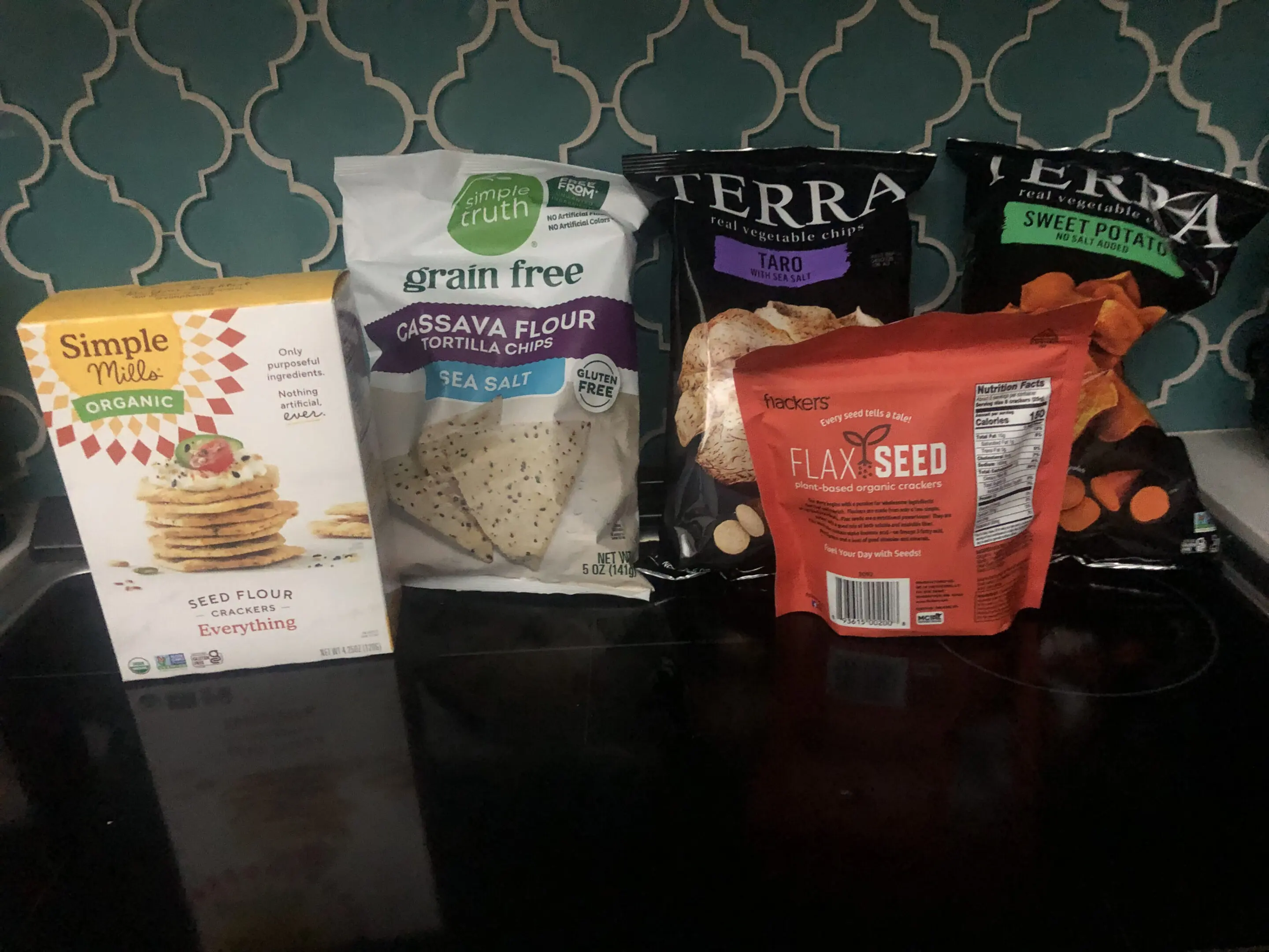 Various packaged food items arranged on a dark surface against a patterned wall.